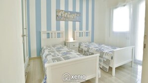 A bedroom with two beds, striped wallpaper, a painting, and a chandelier.