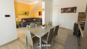 A modern living room with a sofa, a dining table with chairs, and a kitchen area.