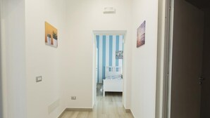 Un pasillo con una cama al fondo, una puerta a la derecha y un interruptor de luz a la izquierda.