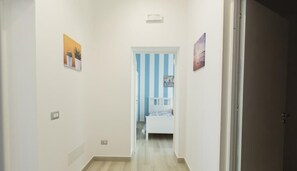 A hallway with a bed at the end, a door on the right, and a light switch on the left.
