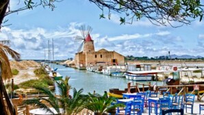 A coastal scene with a windmill, boats, and a dining area with blue chairs and tables.