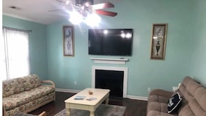 A living room with a sofa, armchair, coffee table, fireplace, TV, and framed artwork. - Cozy Home in Central Morehead 5min. from the Beach (Morehead City)