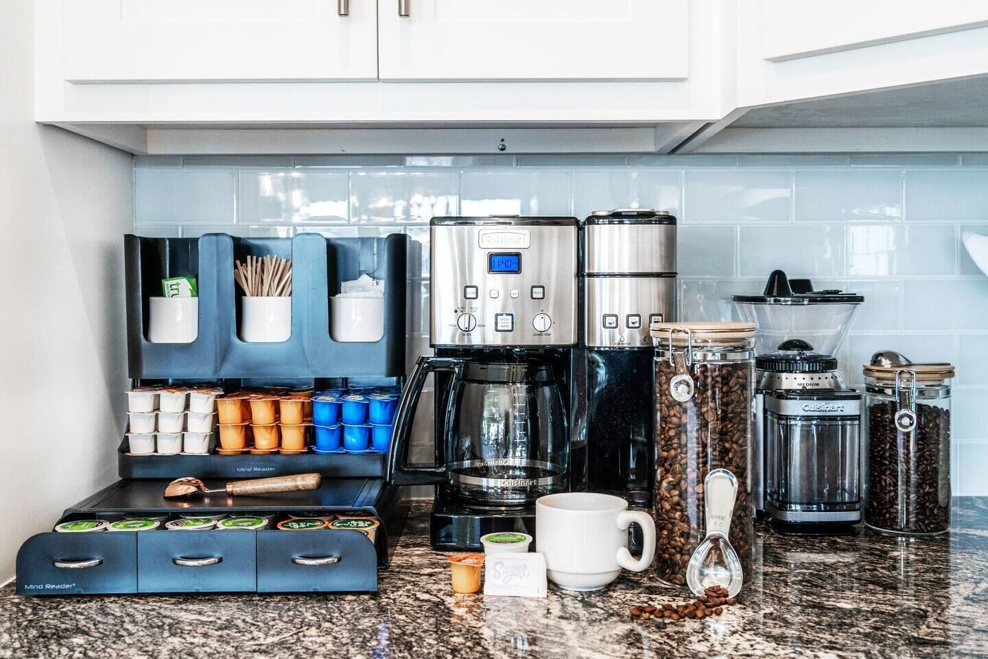 A kitchen with a coffee maker, coffee pods, a grinder, and coffee beans.