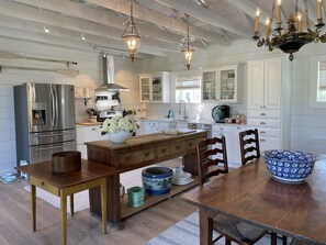 A modern kitchen with a stainless steel refrigerator, wooden dining table, and a large vase of flowers.
