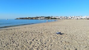 Une vaste plage de sable fin, un ciel bleu dégagé, une mer calme et une ville lointaine avec ses bâtiments.