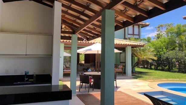 An outdoor kitchen area with a pool and patio furniture. - Beach House Vacation Rental 15 to 22 July 2022 Costa do Sauípe BA (Mata de São João)
