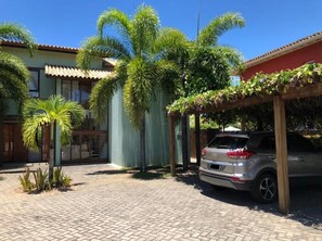 Um caminho de paralelepípedos leva a uma área de estacionamento coberta, com um carro estacionado lá dentro.