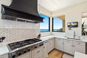 A modern kitchen with a gas stove, white cabinetry, and a large window offering a view of the ocean. - Beachfront Villa, Panoramic Deck & Private Beach (Ponte Vedra Beach)