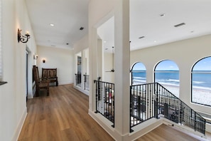 A spacious interior with a wooden floor, a piano, and a balcony with ocean views.