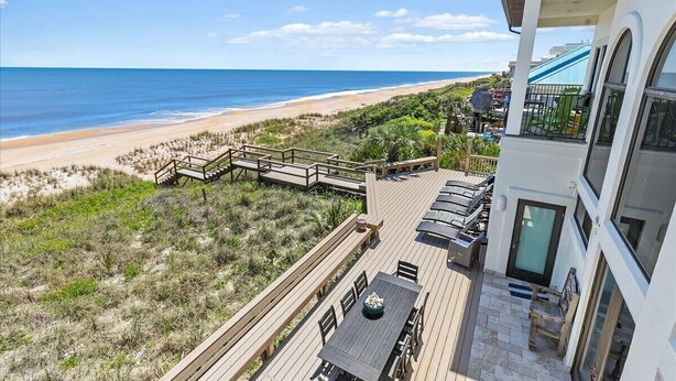 A beachfront property with a wooden deck, outdoor seating, and a view of the beach and ocean. - Beachfront Villa, Panoramic Deck & Private Beach (Ponte Vedra Beach)