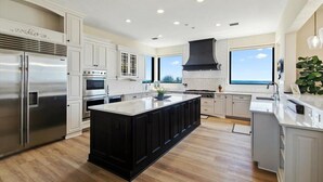 A modern kitchen with white cabinetry, a large central island, stainless steel appliances, and a black range hood. - Beachfront Villa, Panoramic Deck & Private Beach (Ponte Vedra Beach)