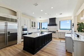 Une cuisine moderne avec des meubles blancs, un grand îlot central, des appareils en acier inoxydable et une hotte noire.