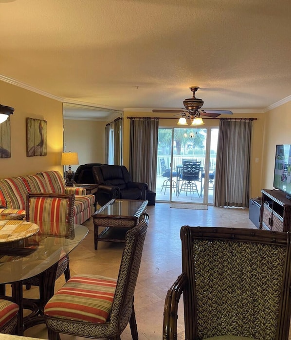 A spacious living room with a dining area, a ceiling fan, and a view to a balcony. - Amalfi Escape (Miramar Beach)