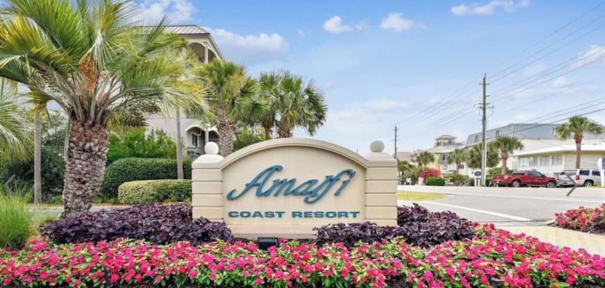 Une enseigne indiquant le « Amati Coast Resort », offrant une vue dégagée sur le paysage environnant, notamment sur les palmiers et une route où circulent des véhicules.