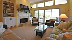 A spacious living room with a fireplace, comfortable seating, and a large window providing natural light. - Private Pool - Litchfield Beach - Second Row (Pawleys Island)