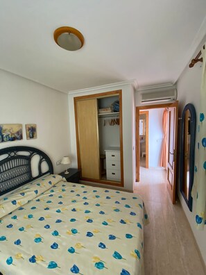 A bedroom with a bed, a wardrobe, a mirror, and a hallway leading to another room.