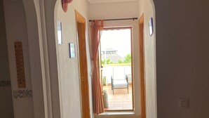 Un corridoio con pavimento piastrellato, una porta in legno e una finestra con tende.