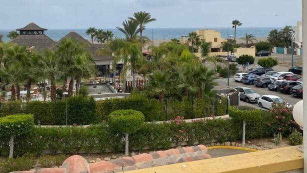 Vista da un balcone su un'area parcheggio, con palme e una spiaggia sullo sfondo.