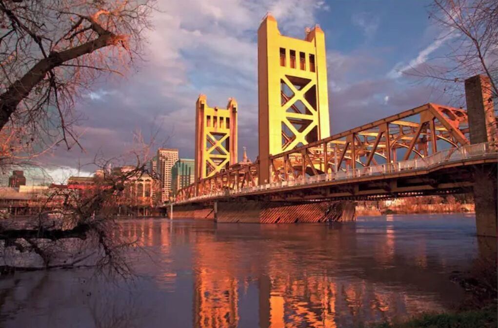 A bridge with two towers, a river below, and buildings in the background.