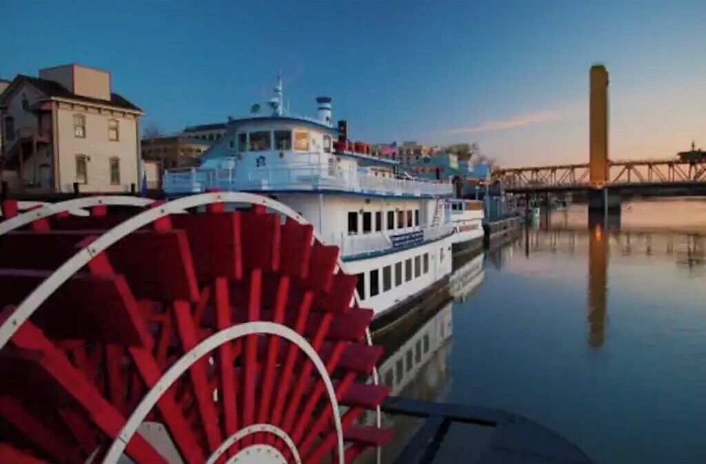 Un bateau à vapeur avec une grande roue à aubes rouge, une cabine blanche et un pont en arrière-plan.