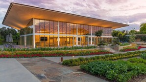 Un bâtiment moderne doté d’une façade en verre et d’un toit plat, entouré de jardins aménagés.