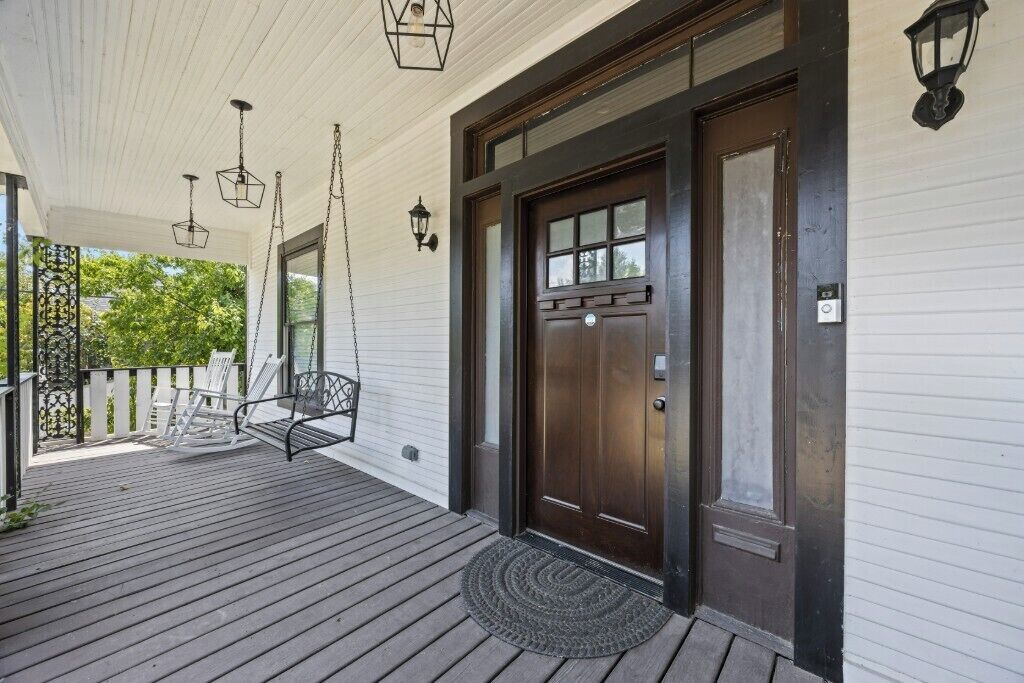 A porch with a wooden floor, a dark brown door, and two hanging lanterns.