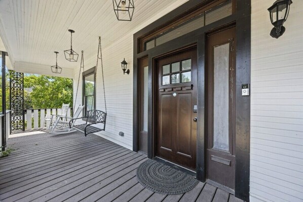 A porch with a wooden floor, a dark brown door, and two hanging lanterns.