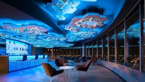 Un salon moderne doté de motifs géométriques au plafond, d’un espace bar et de sièges offrant une vue sur la ville.