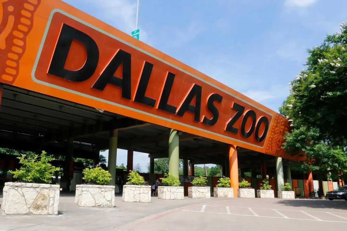 The entrance to the Dallas Zoo with a large sign, stone pillars, and greenery.