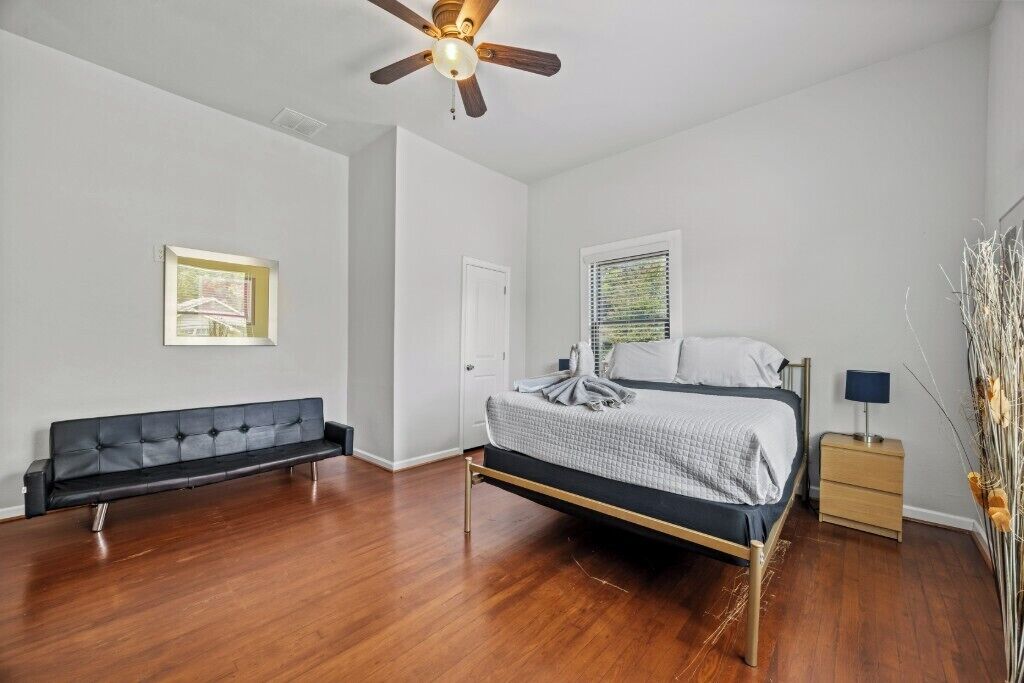 A bedroom with a bed, a bench, a nightstand, a ceiling fan, and a window with blinds.