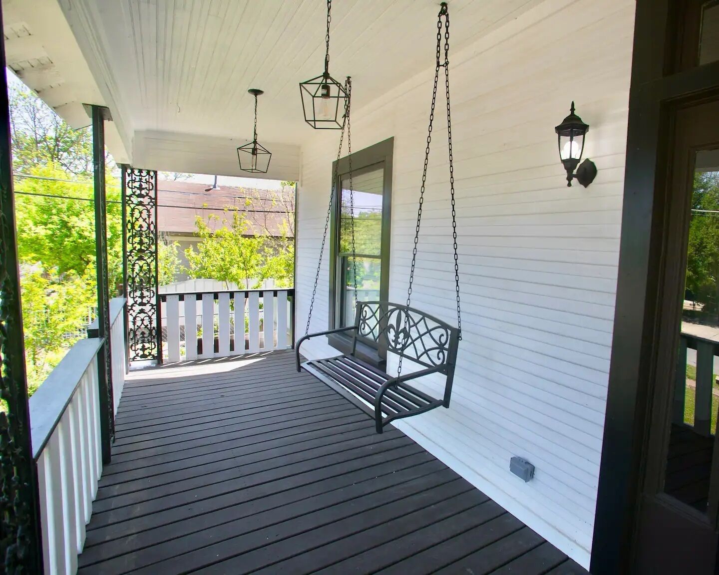 A wooden porch with a black metal swing, white railings, and hanging lanterns.