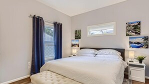 Une chambre à coucher comprenant un lit, des tables de chevet, une fenêtre avec des rideaux et des œuvres d’art murales.