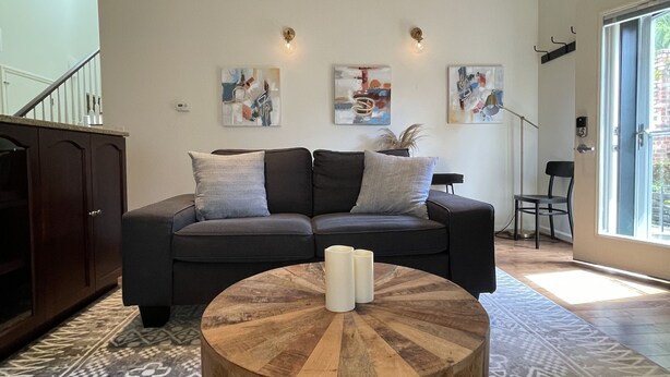 Un salon avec un canapé gris foncé, une table basse ronde en bois et des tapis à motifs.