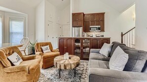 Un salon comprenant un canapé, des fauteuils et une table basse. Il y a également un coin cuisine avec des placards et un four à micro-ondes.