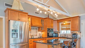 A modern kitchen with stainless steel appliances, wooden cabinets, and a central island with bar stools. - Creek Front Home w/ Fishing Pier & Amazing Outdoor Spaces (Sargent)