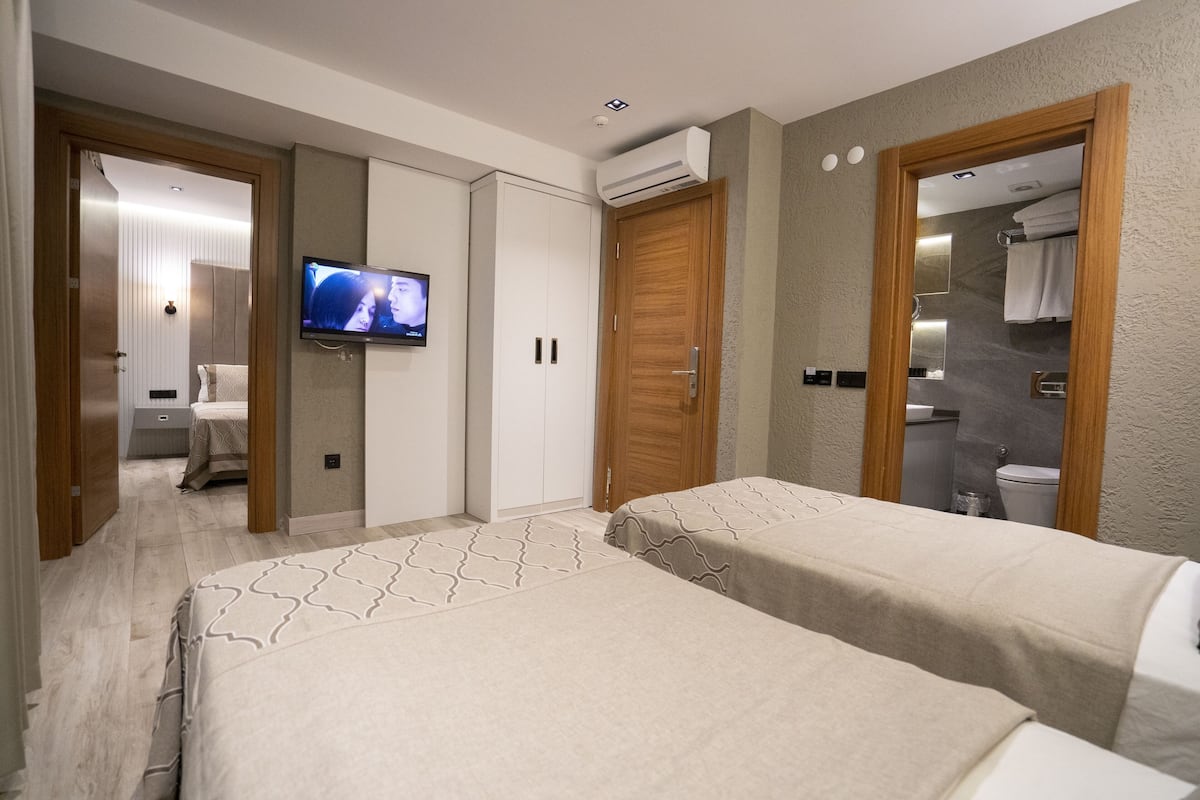 Een hotelkamer met twee bedden, een televisie, een kledingkast en een badkamer met spiegel en handdoekhouder.