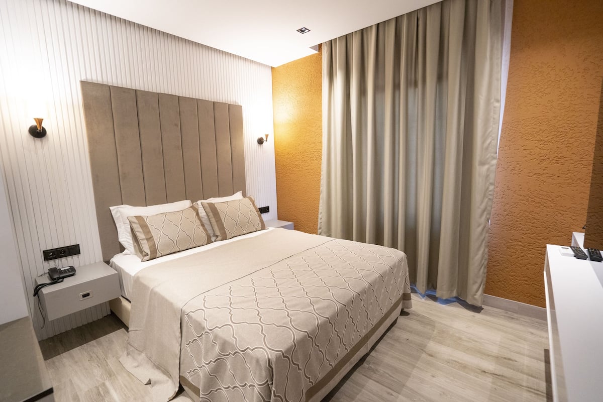 Een hotelkamer met een groot bed, een nachtkastje met een telefoon en een bureau met een computer.