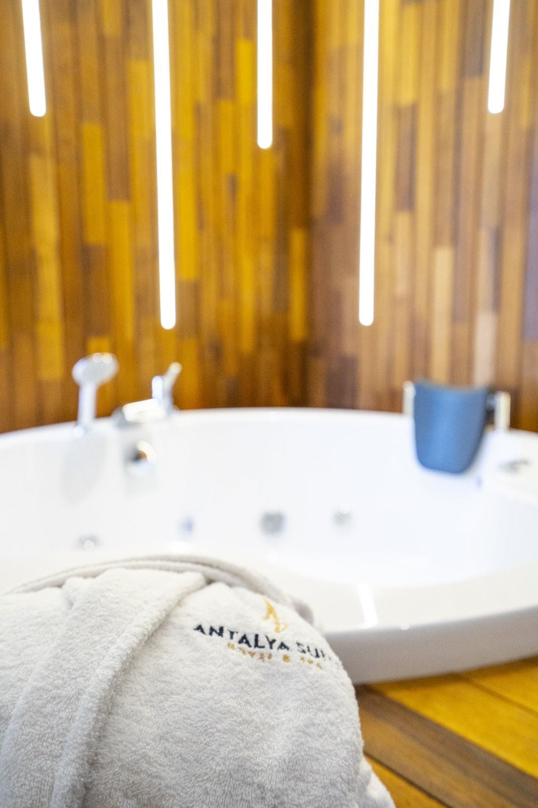 A bathroom with a white bathtub, a blue bucket, and a towel with text.