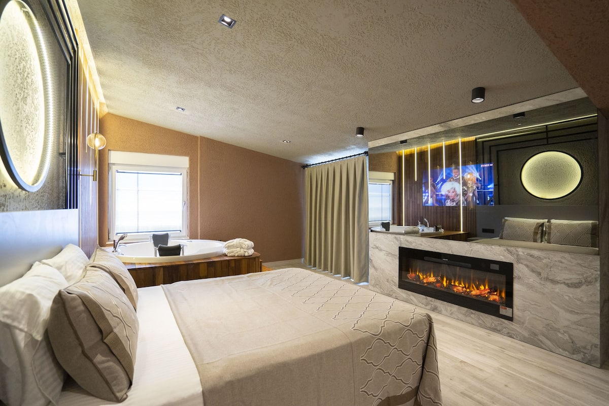 Een moderne hotelkamer met een groot bed, een open haard, een badkamer met bad en een aan de muur bevestigde televisie.