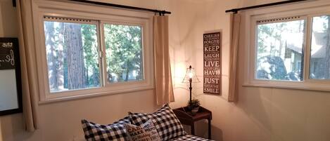 A bedroom with a checkered bedspread, two windows with curtains, a bedside lamp, and motivational wall art.