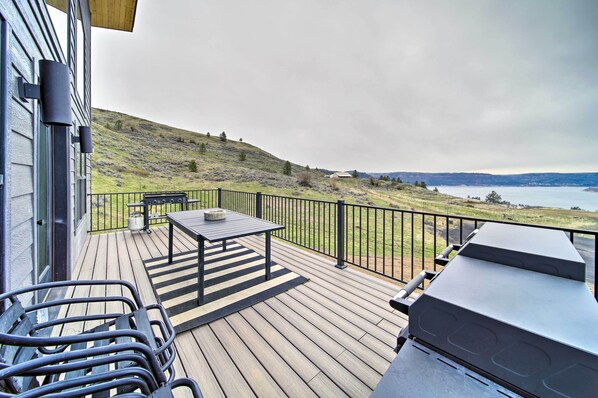 A deck with a table and chairs, a barbecue grill, and a view of a lake and hills. - Modern Davenport Home w/ Water View & Grill! (Davenport)