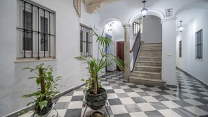 A hallway with a checkered floor, potted plants, a staircase, and a light fixture. - Cadiz Meridian Apartment (Cádiz)