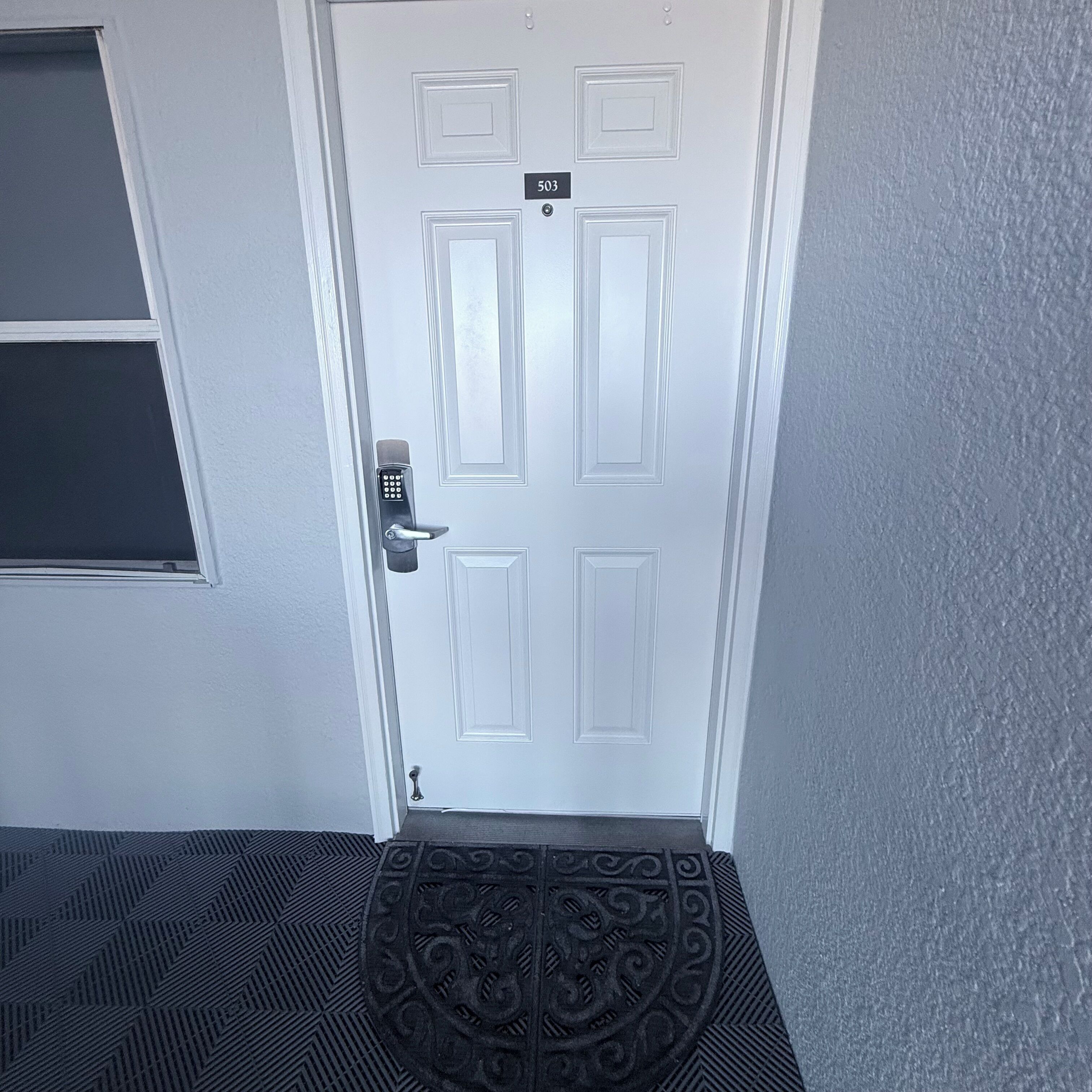 A white door with a keypad lock and a number plate above it.
