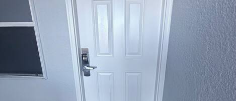 A white door with a keypad lock and a number plate above it.