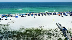 A beach with numerous umbrellas and sun loungers, a wooden walkway, and the ocean in the background.