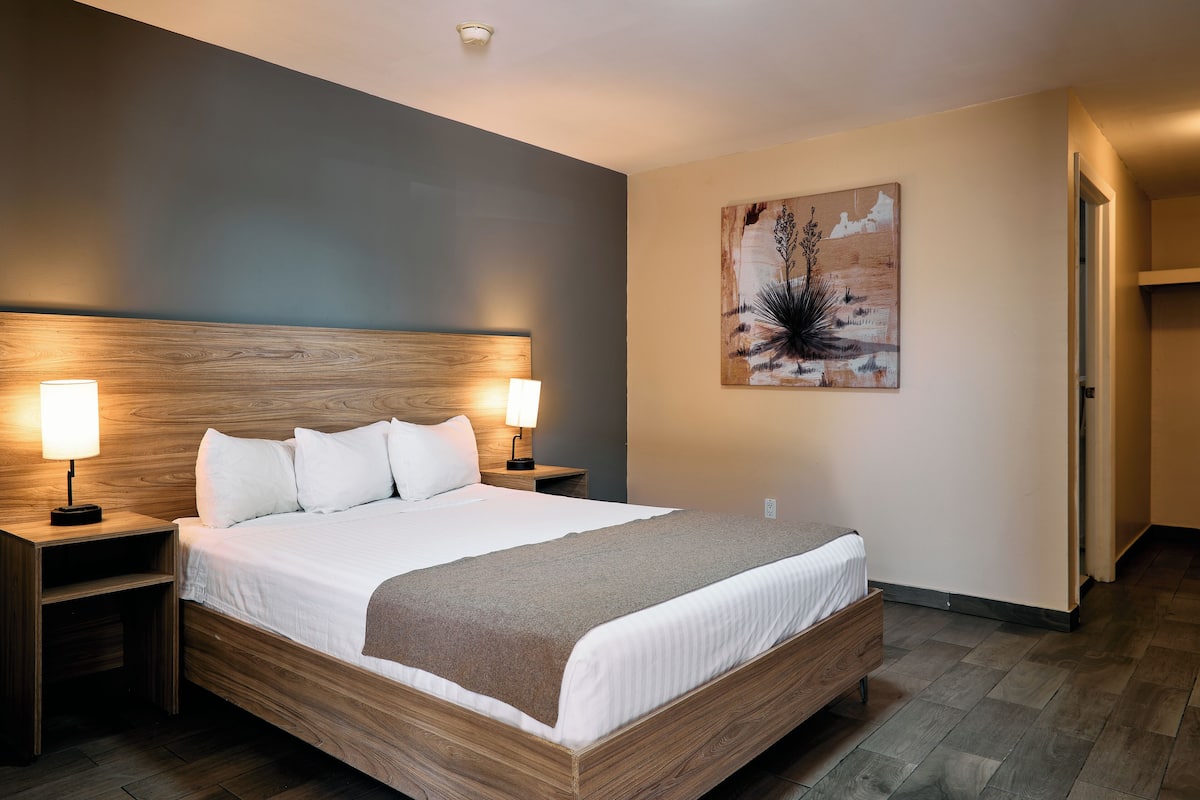Una cama bien tendida con un cabecero de madera, dos lámparas de noche y una obra de arte colgada en la pared.