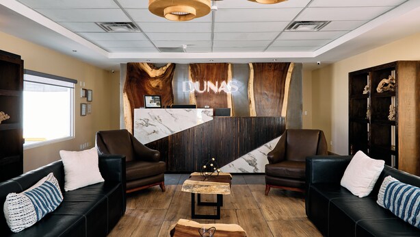 A modern lobby with leather sofas, a reception desk, and a wooden accent wall. - Hotel Dunas (Ciudad Juárez)
