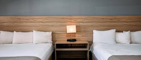 A hotel room with two beds, a nightstand with a lamp, and a wooden headboard.