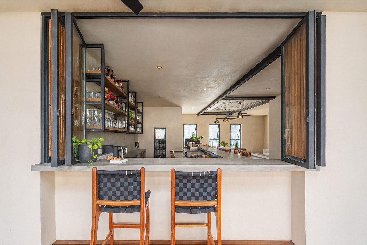 Cocina moderna con barra, sillas de madera, una isla grande y estantes abiertos con utensilios de cocina.