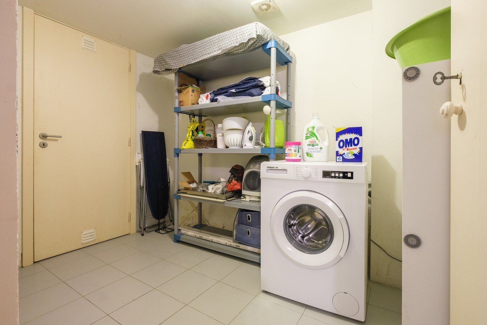 Une buanderie équipée d’un lave-linge, d’étagères contenant des produits de nettoyage et d’une porte.
